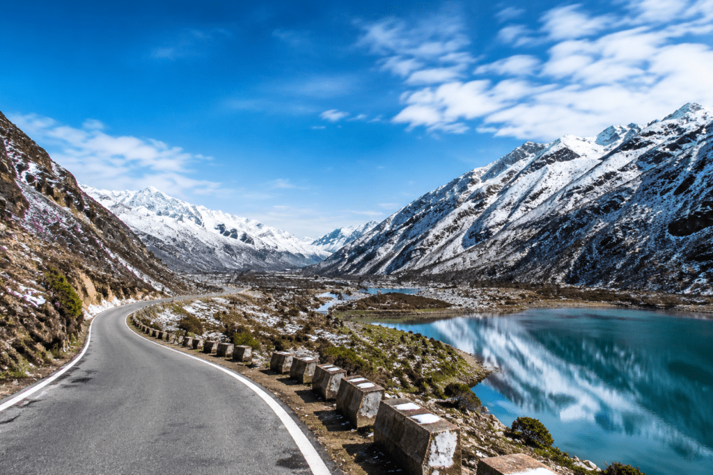 Snow-capped Himalayan mountains with a turquoise lake, winding road, and clear blue sky scenic travel landscape